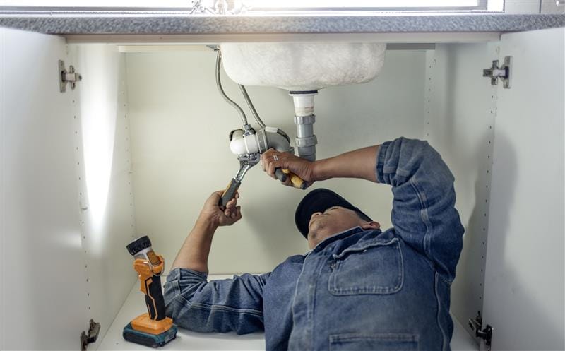 Plumber repairing pipes beneath a bathroom sink in Englewood