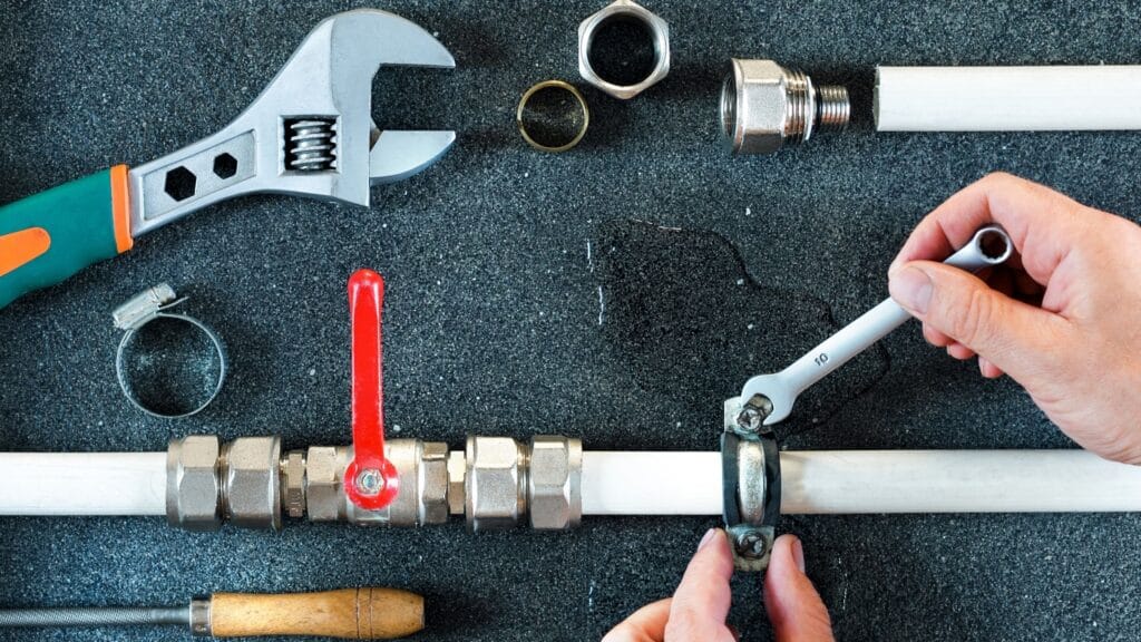 Plumber repairing a pipe valve with an adjustable wrench in Englewood