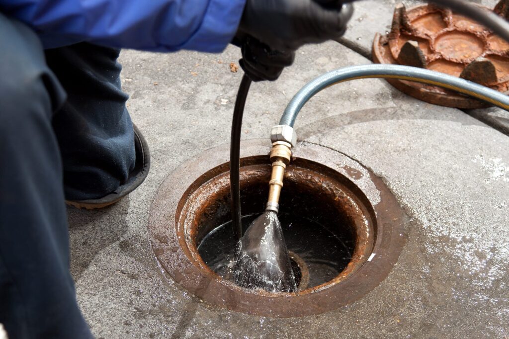 Plumber hydro jetting a sewer line through a manhole in Englewood