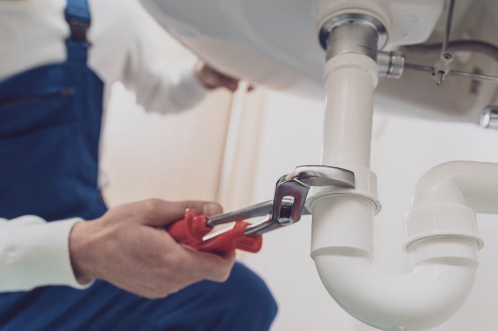 Plumber repairing a white drain pipe beneath a sink in Englewood