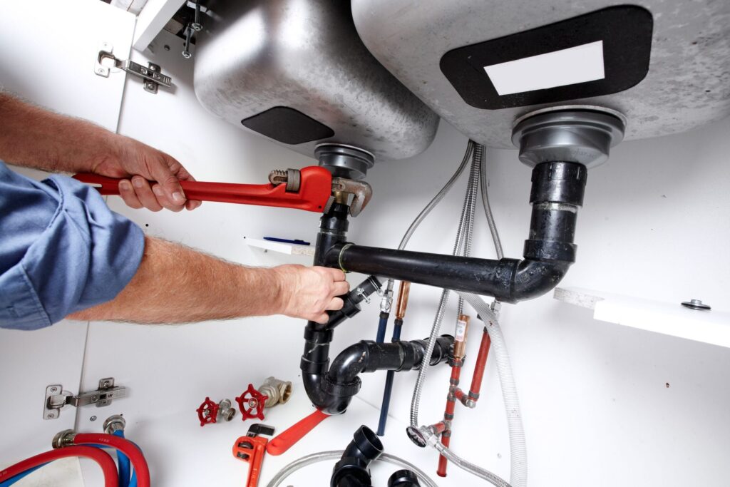 Plumber repairing drain pipes beneath a kitchen sink in Englewood